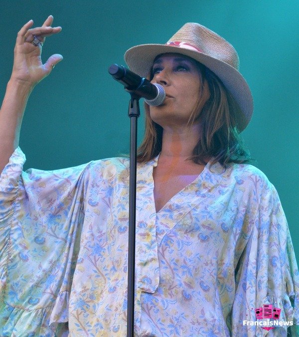 Zazie sur scène en chapeau de paille et robe fleurie, chantant au micro